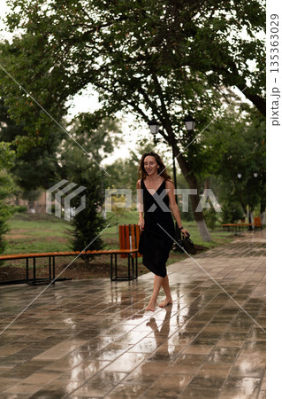 Woman, barefoot, rain, walking happily on a wet park path, embracing a refreshing summer shower 135363029
