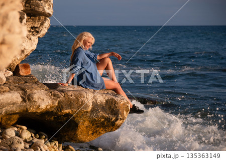 Woman, Beach, Sunset: Blonde woman sits on a rock overlooking the sea at sunset. Woman, Beach, Sunset: Blonde woman sits on a rock overlooking the sea at sunset. 135363149
