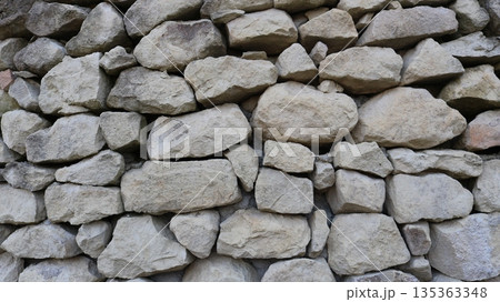 A background texture of natural large solid gray boulders, a full frame, a fragment of a stone fence or wall made of gray rock in the form of rough pieces and blocks A background texture of natural large solid gray boulders, a full frame, a fragment of a stone fence or wall made of gray rock in the form of rough pieces and blocks 135363348