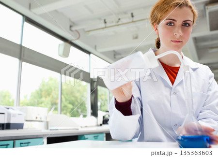 Female scientist holding wash bottle and pouring clear liquid into flask at laboratory bench Female scientist holding wash bottle and pouring clear liquid into flask at laboratory bench 135363603