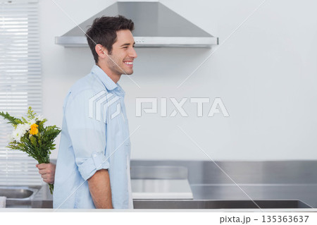 Smiling man turning toward hidden bouquet behind him in home kitchen with steel extractor hood Smiling man turning toward hidden bouquet behind him in home kitchen with steel extractor hood 135363637