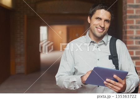 Male student leaning against brick pillar while holding blue tablet in campus corridor, copy space Male student leaning against brick pillar while holding blue tablet in campus corridor, copy space 135363722