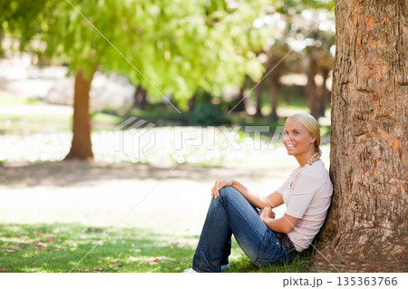 Woman leaning back against large tree trunk on green grass in leafy park, copy space Woman leaning back against large tree trunk on green grass in leafy park, copy space 135363766