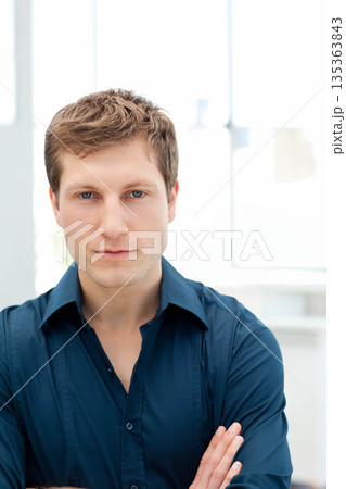 Man standing with crossed arms facing camera in modern office with white window frames 135363843