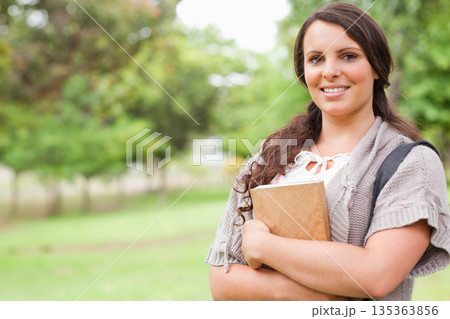 Female student standing in grassy park holding brown-covered notebook wearing backpack, copy space Female student standing in grassy park holding brown-covered notebook wearing backpack, copy space 135363856