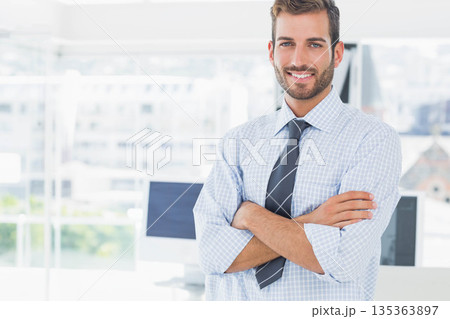 Man in checked shirt and tie crossing arms smiling in office near computer monitors, copy space 135363897