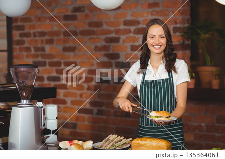 metal tongs placing fresh sandwich on white plate on wooden counter in cozy café, copy space metal tongs placing fresh sandwich on white plate on wooden counter in cozy café, copy space 135364061