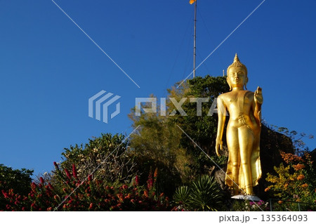 Statues of the old temple.One golden, old Buddha statue of the temple in the blooming garden. Statues of the old temple.One golden, old Buddha statue of the temple in the blooming garden. 135364093