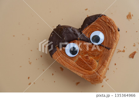 Funny crazy joke eyes on Delicious fresh croissant topped with Dark chocolate flavor Ganache. April fool day concept Creation unique heart shape bakery. Puff pastry holiday love gift present idea Funny crazy joke eyes on Delicious fresh croissant topped with Dark chocolate flavor Ganache. April fool day concept Creation unique heart shape bakery. Puff pastry holiday love gift present idea 135364966