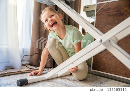 Young girl playing under piano at home after music lesson. Childhood spontaneity and playful behavior during home education process. 135365513