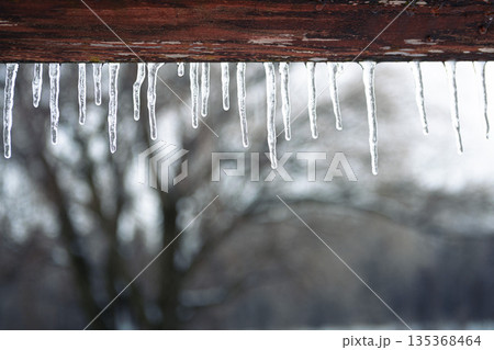 A close-up shows sharp icicles forming along a wooden roofline. 135368464