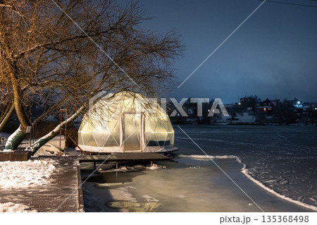 Modern illuminated dome structure on a frosty river bank. Winter luxury relaxation. Modern illuminated dome structure on a frosty river bank. Winter luxury relaxation. 135368498