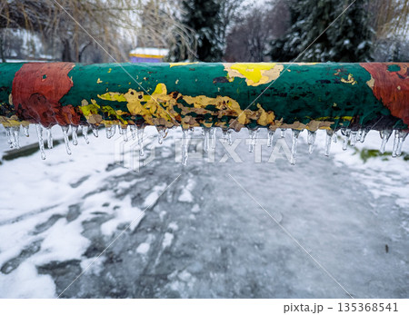 A close-up of a multi-colored metal barrier covered with frost, ice and hanging icicles 135368541