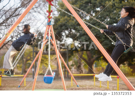 冬の夕方の公園でブランコを遊んでいる可愛い女子中学生姉妹の姿 135372353
