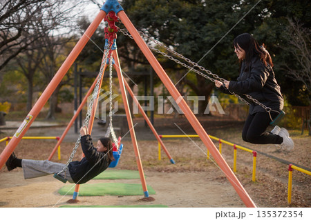 冬の夕方の公園でブランコを遊んでいる可愛い女子中学生姉妹の姿 135372354