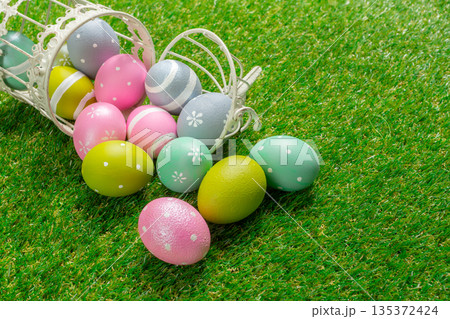 Colorful easter eggs scattered on grass near a small basket during spring season 135372424