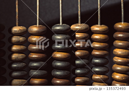 Wooden beads are strung on metal rods in a dark setting under a light 135372493