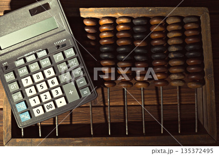 Calculator and abacus sit on a wooden surface in a study space during afternoon light Calculator and abacus sit on a wooden surface in a study space during afternoon light 135372495