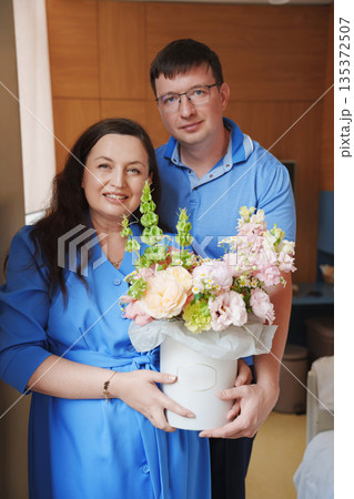 Couple holds a flower arrangement at a home setting Couple holds a flower arrangement at a home setting 135372507