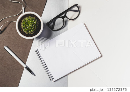 Items on a desk including a notepad, plant, glasses, and a pen 135372576