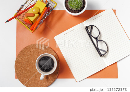 Workspace with coffee, notebook, glasses, and organizational items on a desk 135372578
