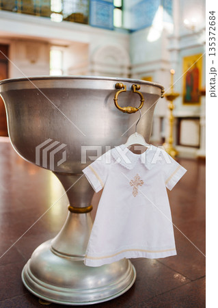 Baptism dress hangs near silver baptismal font Baptism dress hangs near silver baptismal font 135372684