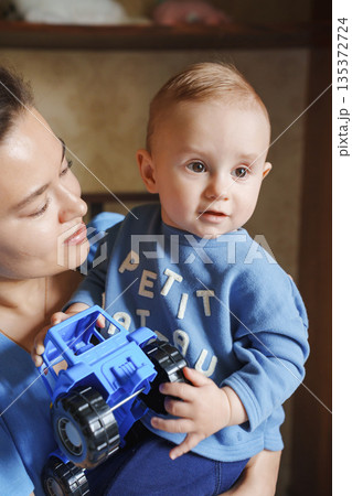 Baby with toy truck smiles while being held by mother 135372724