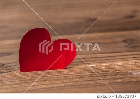 Red paper heart stands on a wooden surface showing love and affection in a simple setting Red paper heart stands on a wooden surface showing love and affection in a simple setting 135372737