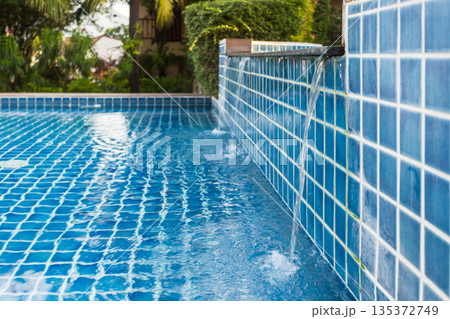 Water flowing into a swimming pool with blue tiles in a garden setting during daytime 135372749