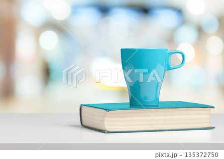 Cup of beverage placed on a book in a bright indoor space with blurred background Cup of beverage placed on a book in a bright indoor space with blurred background 135372750