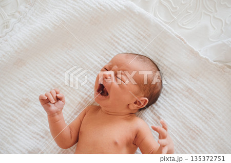 Newborn baby yawning on a soft blanket in a room 135372751