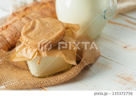 Milk and cheese sit on a wooden table with bread nearby in a rustic kitchen setting Milk and cheese sit on a wooden table with bread nearby in a rustic kitchen setting 135372756