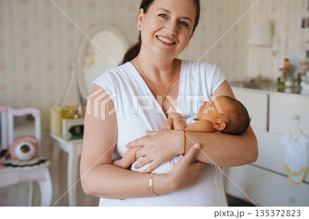 Mother holds newborn baby in cozy room setting Mother holds newborn baby in cozy room setting 135372823