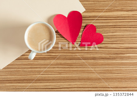 Coffee sits next to red paper hearts on a wooden table during morning time 135372844