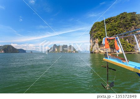 Boat anchored near green rocks and blue water in a tropical area on a sunny day Boat anchored near green rocks and blue water in a tropical area on a sunny day 135372849