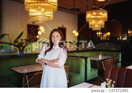 Woman in white dress stands confidently in cozy restaurant 135372891