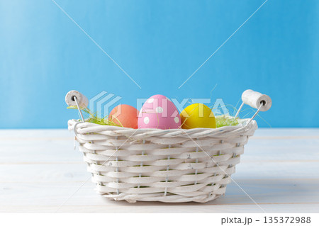 Colorful eggs in a white basket on a blue background during spring season 135372988