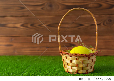 Basket with yellow egg on grass in a wooden setting for spring activity 135372990