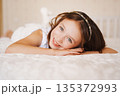 Young girl smiles while lying on bed in bright room 135372993