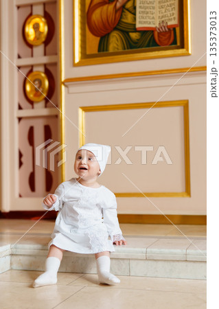 Child in a white dress sitting by religious artwork Child in a white dress sitting by religious artwork 135373013
