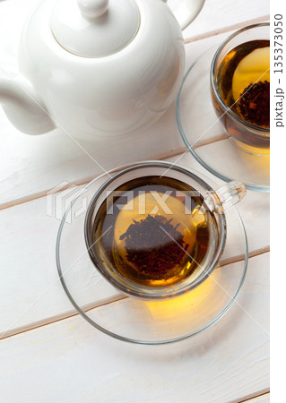 Hot tea is served in glass cups with a white teapot on a wooden table Hot tea is served in glass cups with a white teapot on a wooden table 135373050