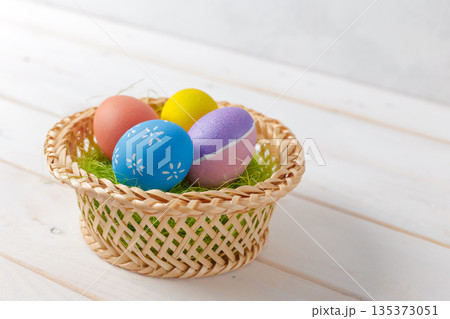 Colorful eggs in a basket on a white wooden table for a spring event Colorful eggs in a basket on a white wooden table for a spring event 135373051