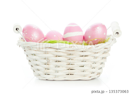 Colorful eggs in a white basket with green grass on a plain background 135373063
