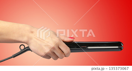 Person holds a hair straightener with a red background during a beauty routine Person holds a hair straightener with a red background during a beauty routine 135373067