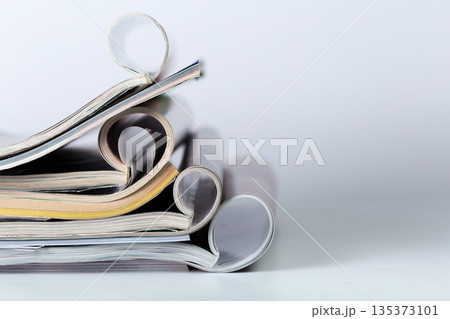 Close-up of magazines with curled pages on a flat surface arranged in a neat stack 135373101