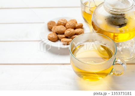 Hot tea in a cup next to a plate of cookies on a white wooden table 135373181