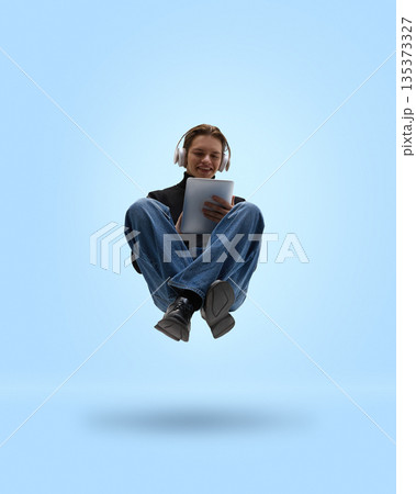 Casual man levitating with tablet and headphones on blue background. 135373327