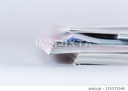 Stacked magazines resting on a white surface with blurred background in a simple setup 135373340