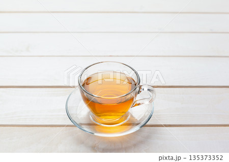 Freshly brewed tea in a clear cup resting on a white wooden table 135373352