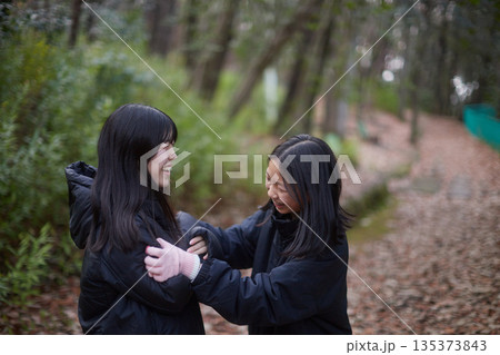 冬の朝の公園で楽しく散歩しながら遊んでいる女子中学生姉妹の姿 135373843